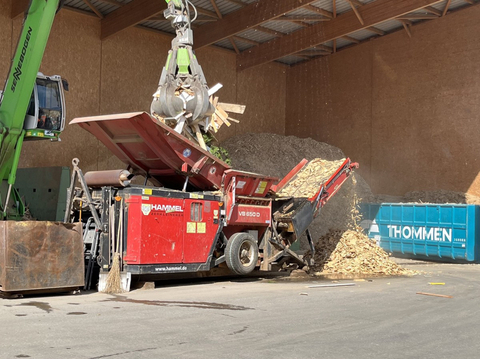 Greifbagger beladet Holzshredder mit Altholz. Thommen-Container im Hintegrund.