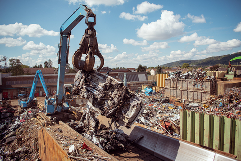 Greifbagger befördert Altkarosse auf das Einzugsplattenband vom Shredder
